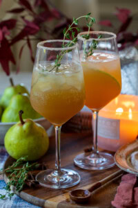 Refreshing pear cocktails with fresh herbs on a wooden serving board, perfect for summer drinks.