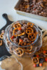 Halloween Muddy Buddies with chocolate-coated Rice Chex, mini pretzels, Oreos, and orange and black M&M's in a glass pumpkin jar.