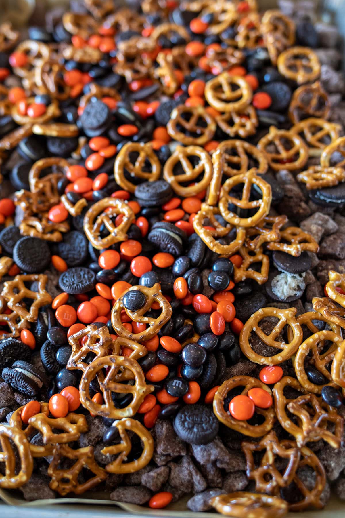 Halloween Muddy Buddies with chocolate-coated Rice Chex, mini pretzels, Mini Oreos, and orange and black M&M's party mix.